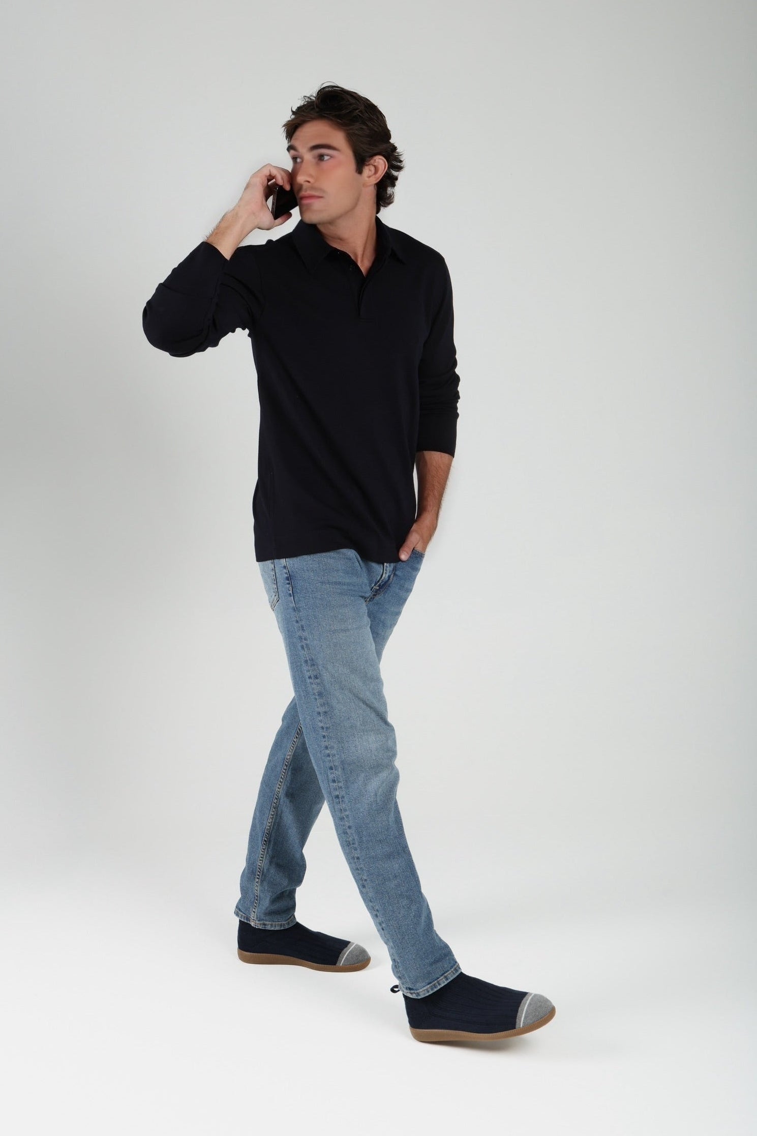 Man wearing a black shirt and light blue jeans, standing against a white background